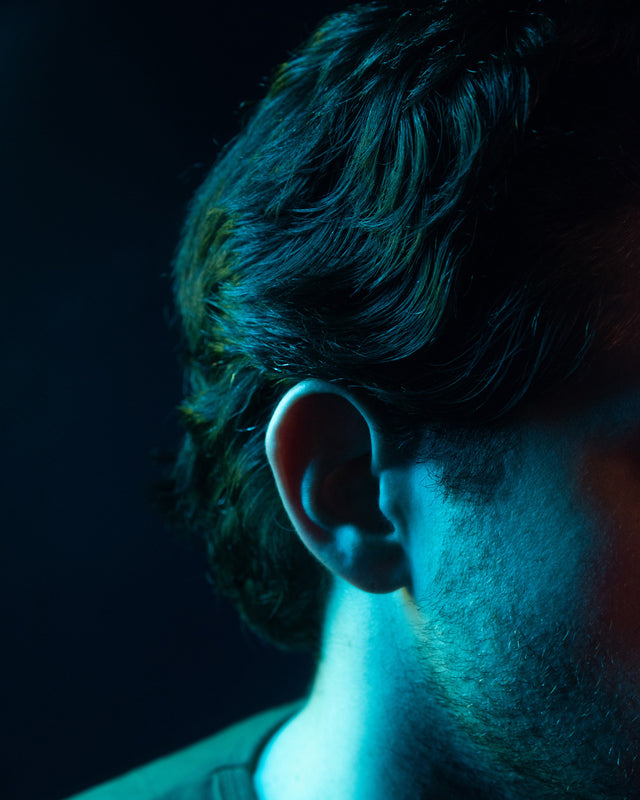 A close up of a person's side profile, scruff, and hair in in vibrant lighting.