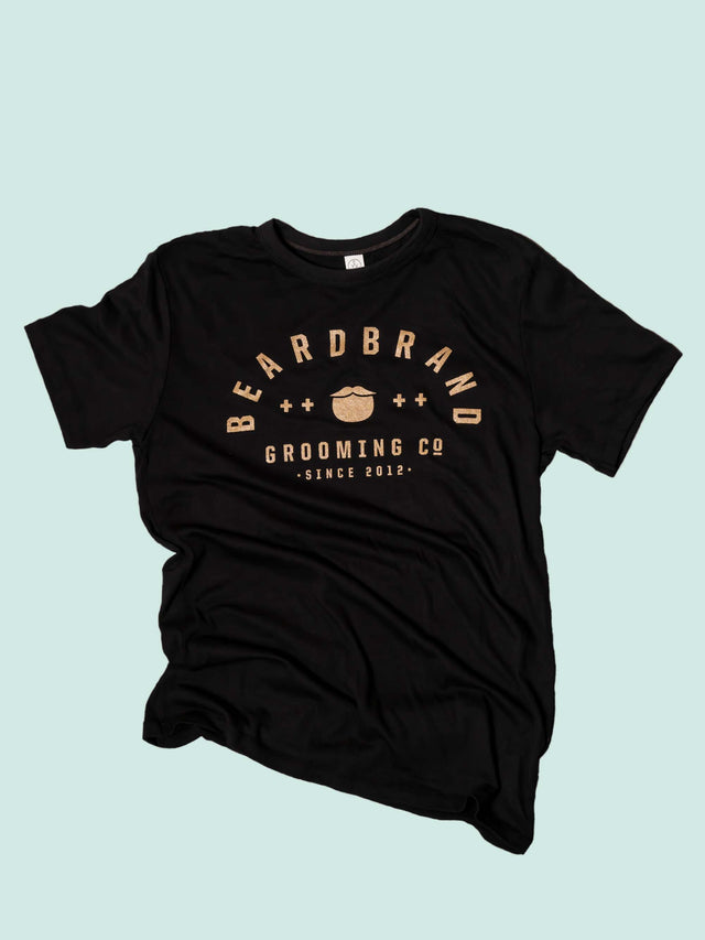 A faded black, “Dark Smoke” Beardbrand Banner Tee with gold ink print on the front.